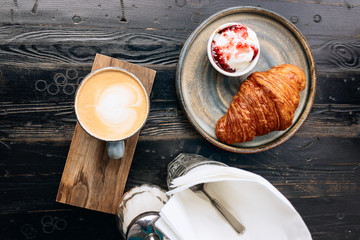 Coffee, croissant and ice-cream with strawberry jam on stone plate on black wooden table. Tasty background.
