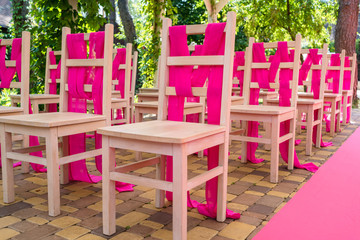 Wedding chairs on each side of archway with pink cloth. Place for wedding ceremony decorated in pink color,  wooden chairs for guests outdoors. Wedding ceremony in pink color