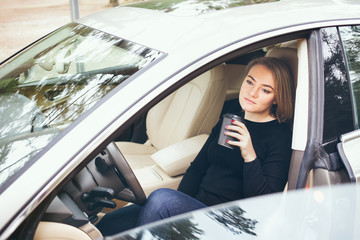 Woman resting in the car from a long journey and drinking takeaway cup of hot coffee, to boost energy.