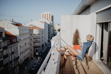 Fototapeta premium Young and beautiful woman sitting in the chair on the balcony at morning