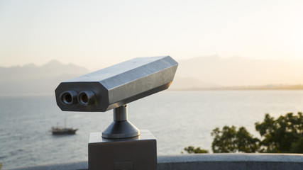 binocular tower viewer pointing to sea, with boat and mountains in the background