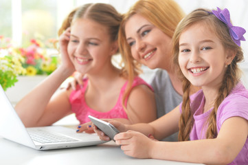 Mother and  girls sitting at  table and using  laptop