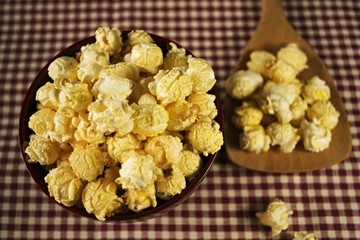 Popcorn in a wooden bowl and in a wooden ladle. On checkered pattern Focus in the bowl