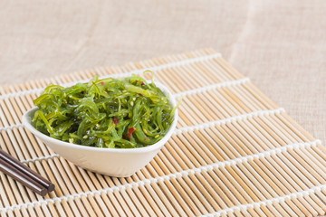 wakame seaweed salad in a ceramic bowl on bamboo mat. popular and delicious japanese food appetizer.