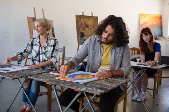 Adult students painting on book while sitting at table