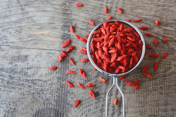 Goji berries fruit on colander and wooden table in the background.