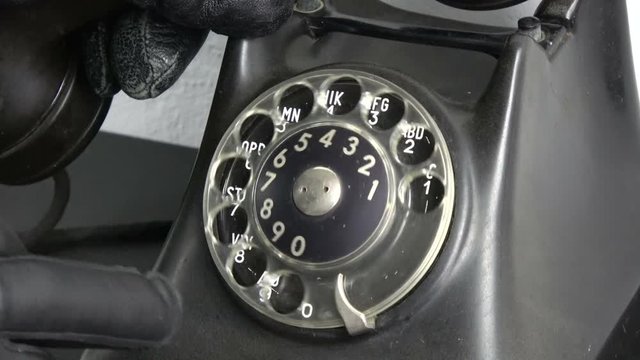 Gangster thief hand with black leather glove dialing old phone telephone dial disc