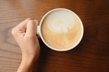 top view. hand of young woman hold cup with coffee have wood table are background. this image for beverage,drink,food,body part,business concept