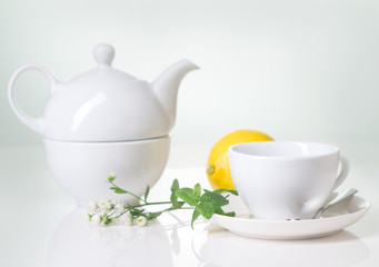 White teacup, teapot with herbal tea and lemon