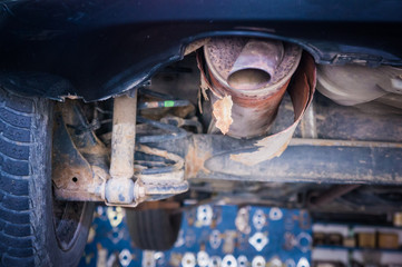 Worn out exhaust pipe on lifted car in the workshop.
