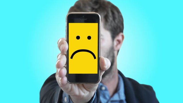 Man Shows Sadness Through Smartphone. Man shows his feelings through a smartphone with a sad Smiley face on screen