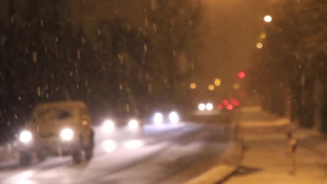 Nevando copiosamente en una calle de noche, con coches en movimiento que se acercan y alejan. Fuera de foco o desenfocado
