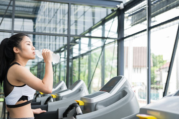 Fototapeta na wymiar young woman drinking water in fitness center. female athlete feeling thirsty after training in gym. sporty girl taking a break from working out in health club.