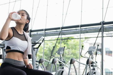 young woman drinking water in fitness center. female athlete feeling thirsty after training in gym. sporty girl taking a break from working out in health club.