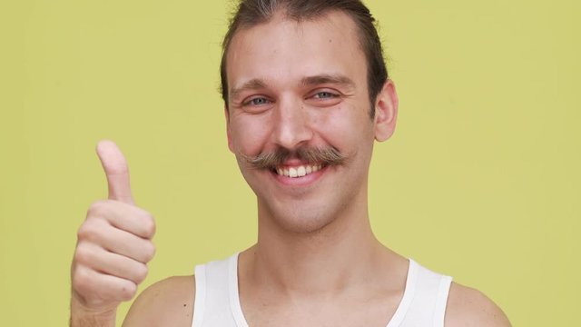 Portrait of funny caucasian man smiling over yellow background making face while twirling mustaches closeup. Concept of emotions