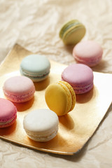 Colorful macarons on a golden plate. French sweets assortment viewed from above on a neutral paper background