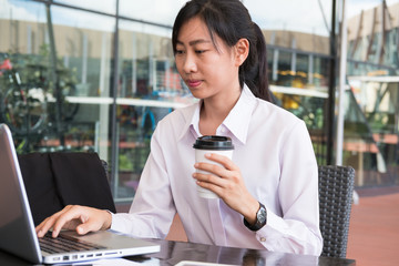 businesswoman with laptop computer sitting outside office building. young asian woman analyzing investment charts outdoors. business people with coffee woking online