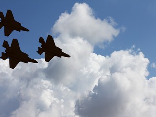 Silhouettes of three F-35 aircraft against the blue sky and white clouds