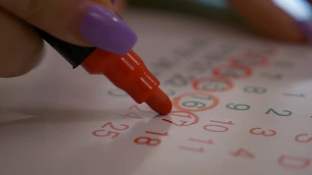 Female hand marking dates on calendar planning birth control