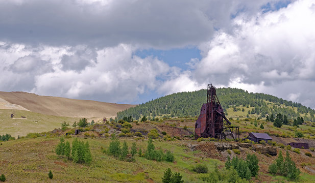 Equipment remains of 19th Century deep gold mining operations near Victor, Colorado, U.S.A. with spoil from the current Cripple Creek Mining District open cast gold mine in the background