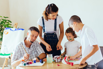 Family with two kids painting together at home, happy mother, father and children. Smiling family drawing together in kitchen at home. New housing, art and family leisure concept.