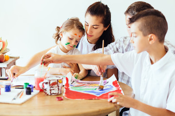 Family with two kids painting together at home, happy mother, father and children. Smiling family drawing together in kitchen at home. New housing, art and family leisure concept.