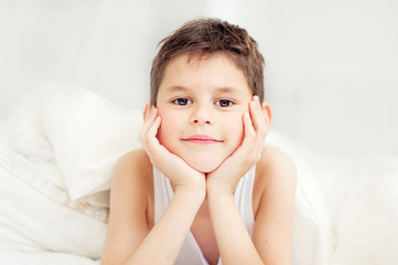 Cute boy under a blanket in bed in the bedroom. Lying on bed.  The concept of awakening and the time of sleep.  Portrait of a close-up with an instagram filter