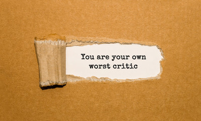 The text You are your own worst critic appearing behind torn brown paper