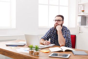 Pensive young businessman takes notes in modern white office