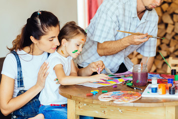 Mother with little girl painting together at home, happy mother, father and child. Smiling family drawing together in kitchen at home. New housing, art and family leisure concept.