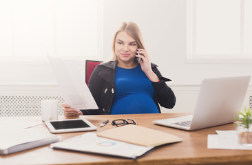 Pregnant business woman talking on phone at office