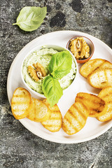 Appetizing crispy toasted grilled toasts with feta paste with walnuts, herbs, salt, garlic, fresh basil in ceramic ware on a gray stone background. Top view..