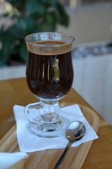 Glass cup of a black coffee with milk on a wooden table