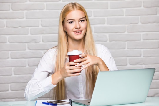 Attractive blond business woman working on her laptop and drinking coffee in her office