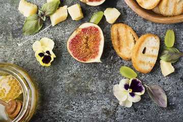 Ingredients for appetizing sandwiches for breakfast or snacks from grilled bread, figs, cheese, grapes, honey and nuts on a gray stone background with edible flowers. Top view.
