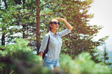 Young woman with backpack standing on cliff's edge and looking to a sky