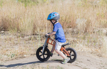 Fototapeta premium Toddler on a Strider Bike at a Dirt Track Wearing Helmet
