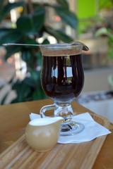 Glass cup of a black coffee with milk on a wooden table