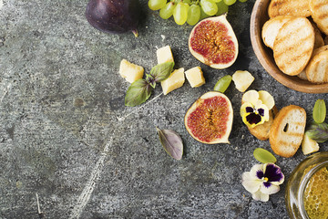 Ingredients for appetizing sandwiches for breakfast or snacks from grilled bread, figs, cheese, grapes, honey and nuts on a gray stone background with edible flowers. Top view.