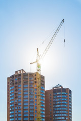Fototapeta premium Building crane and building under construction against a blue sky in the sunlight