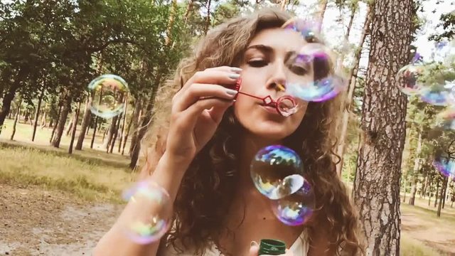 Charming girl blowing soap bubbles in park in summer