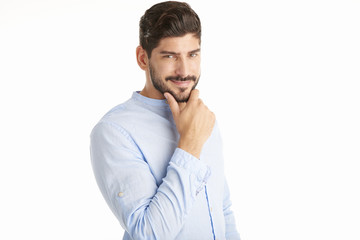 Thinking young man with hand on chin standing against at isolated white background and looking at camera.