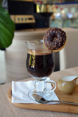 Black coffee with milk in a glass cup on a wooden table