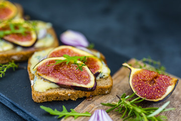 Baked toast of dark bread with blue cheese and figs served on cutting board.