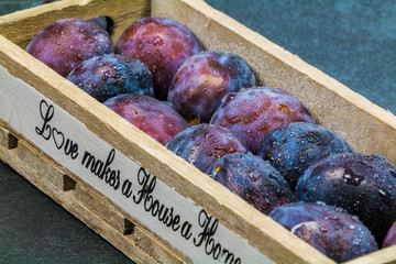 fresh plums with waterdrops on it in a wooden box