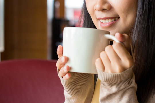 Asian woman holding white cup of coffee with both hand close to her mouth