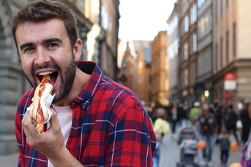 Young man eating a hot dog outdoors