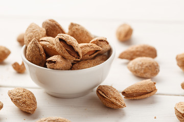 Heap of almond in shell in a white bowl on a wooden table