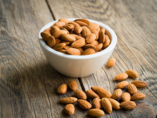 white bowl with a handful of nuts of almonds on a wooden background table. Image with shadow.