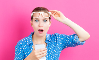 Young woman using her phone on a pink background